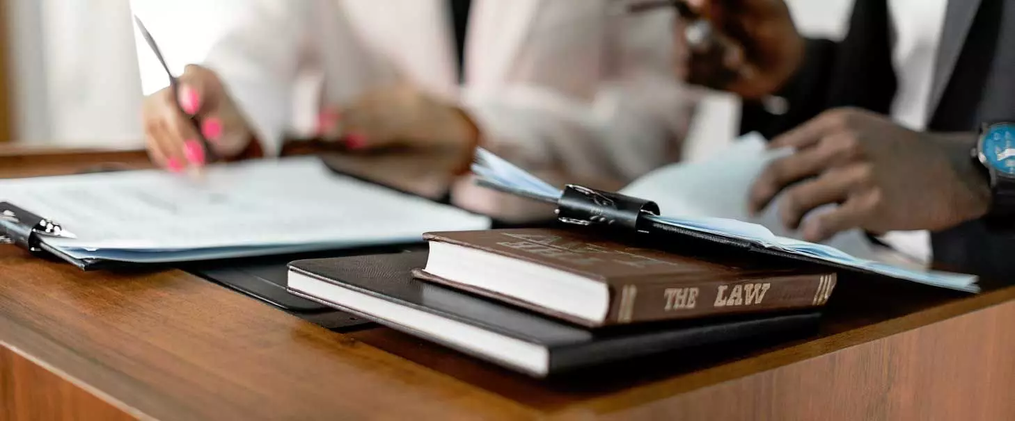 An image of a desk with a book titled The Law and other paperwork being looked at by two individuals sitting side by side